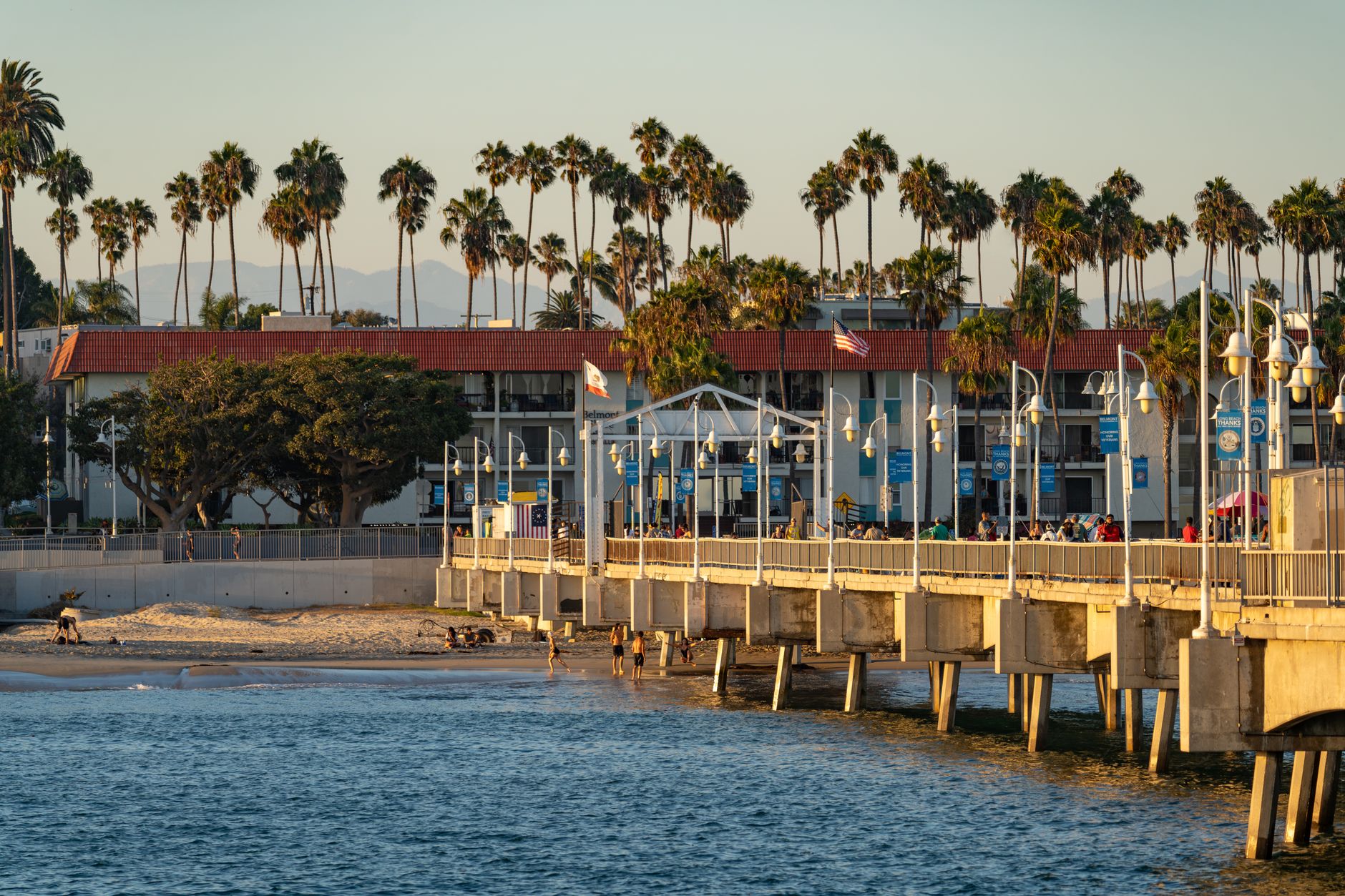 A serene view of Santa Monica Pier during sunset, featuring palm trees and beachgoers